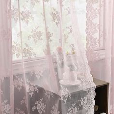 a white teddy bear sitting on top of a table in front of a sheer curtain