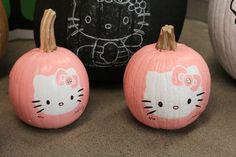 two hello kitty pumpkins sitting next to each other on a table with an chalkboard in the background