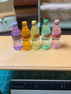 a group of six different colored bottles sitting on top of a table next to a ruler