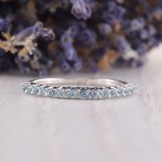 a white gold wedding band with blue topazte stones on the side and lavender flowers in the background