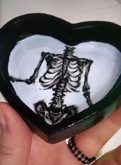 a hand holding a heart shaped box with a skeleton painted on the front and side