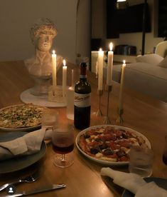 a table topped with pizzas and candles next to a bottle of wine on top of a wooden table