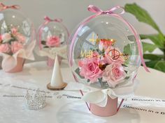 three vases filled with pink flowers on top of a white table covered in paper