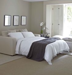 a white bed sitting in the middle of a bedroom next to a window with pictures on it