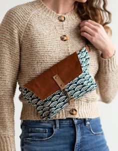 a woman in jeans and a sweater holding a brown purse with an interesting design on it