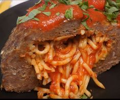 a piece of meatloaf with spaghetti and tomato sauce on a black plate topped with parsley