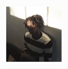 a man with dreadlocks sitting against a wall