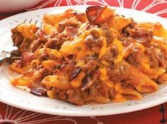 a white plate topped with pasta and meat covered in sauce next to a bowl of carrots