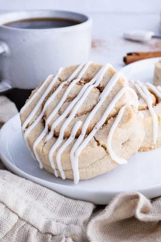 two cookies with white icing on a plate next to a cup of coffee and cinnamon sticks