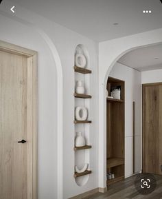 a white room with wooden floors and shelves filled with decorative objects on the wall, along with an arched doorway that leads to another room