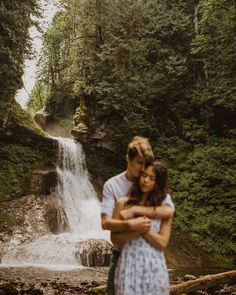 a man and woman hugging in front of a waterfall