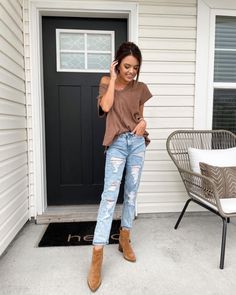 a woman is standing on the porch talking on her cell phone while wearing ripped jeans and brown boots