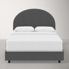 an upholstered bed with white pillows and gray headboard, against a grey wall