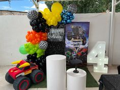 a birthday party with balloons and toys on the ground next to a sign that says happy birthday, monster jam