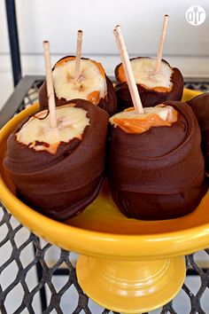 chocolate covered apples with caramel toppings in a yellow bowl on a black and white table