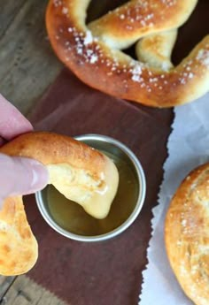 a person dipping something into a small bowl with some bread in it and another bagel on the side