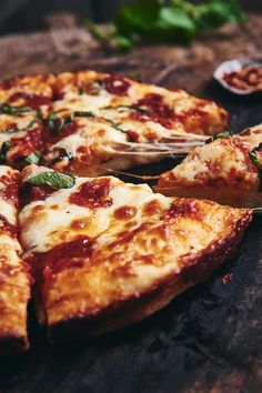 a pizza sitting on top of a wooden table next to a slice of pizza with cheese and spinach