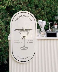 the martini bar is set up outside in front of some trees and shrubbery with glasses on it