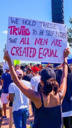 a woman holding up a sign that says we hold these truths to be self - exident that all men are created equal