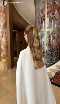 a woman with long hair wearing a white cape and standing in front of a staircase