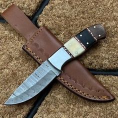 a knife is laying on the ground next to a brown leather sheath with black stitching