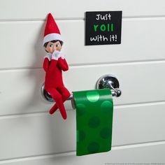 an elf is hanging on the wall next to a roll of toilet paper