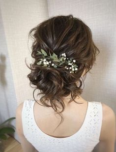 the back of a woman's head with flowers in it and greenery on her hair