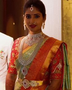 a woman in an orange and green sari with jewelry on her neck, standing next to a man