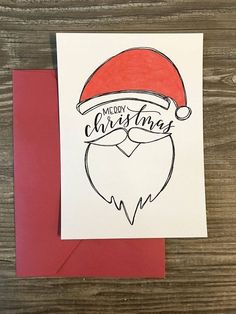 a christmas card with a santa hat and beard drawn on it, next to a red envelope