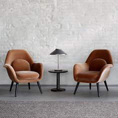 three chairs are lined up against a white brick wall, one has a lamp on it