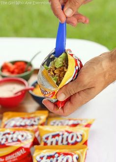 a person is holding a bag of chips in front of some other snacks on a table