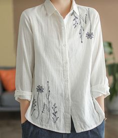 a woman standing in front of a couch wearing a white shirt with blue flowers on it