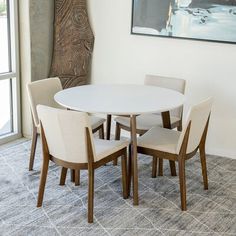 a dining room table and chairs in front of a large window with a painting on the wall