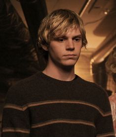 a young man with blonde hair standing next to a woman in a black and brown sweater