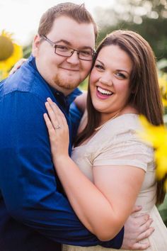 a man and woman hugging each other in front of sunflowers