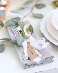 the place setting is set with silverware, napkins and greenery on it