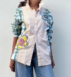 a woman standing in front of a white wall wearing jeans and a shirt with patches on it