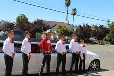 a group of men standing next to each other in front of a white car with red bow ties