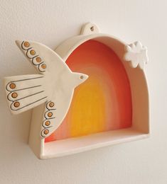 a white ceramic bird with orange and yellow colors on it's wings is mounted to the wall