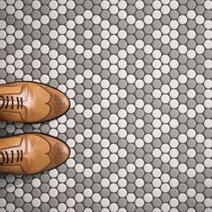 a pair of brown shoes sitting on top of a white and gray tile covered floor