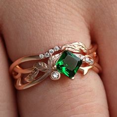 a close up of a person's hand wearing a ring with an emerald stone