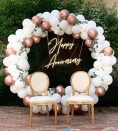 two chairs sitting in front of a white and rose gold balloon arch with greenery