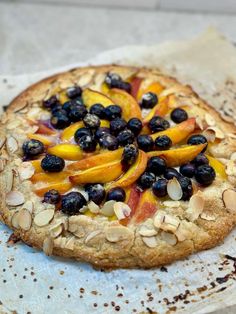 a pizza with blueberries, peaches and almonds on it sitting on a piece of parchment paper