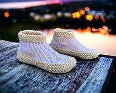 a pair of white knitted slippers sitting on top of a wooden table next to a body of water