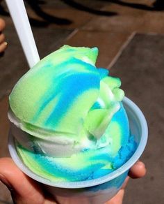 a hand holding a cup filled with green and blue swirled ice cream