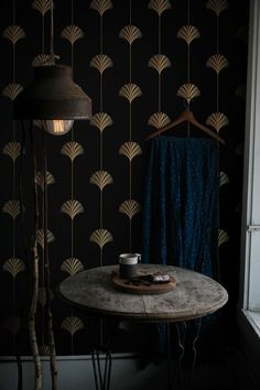 a table with a cup on it in front of a wallpapered background and lamp