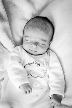 a black and white photo of a baby sleeping on a blanket with his eyes closed