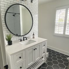 a bathroom with black and white tile flooring and a round mirror above the sink