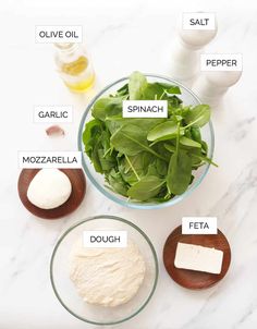 ingredients for spinach salad laid out in bowls on a marble counter top with names