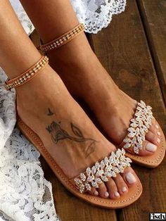 a woman's feet with tattoos and sandals on top of her legs, sitting on a wooden floor